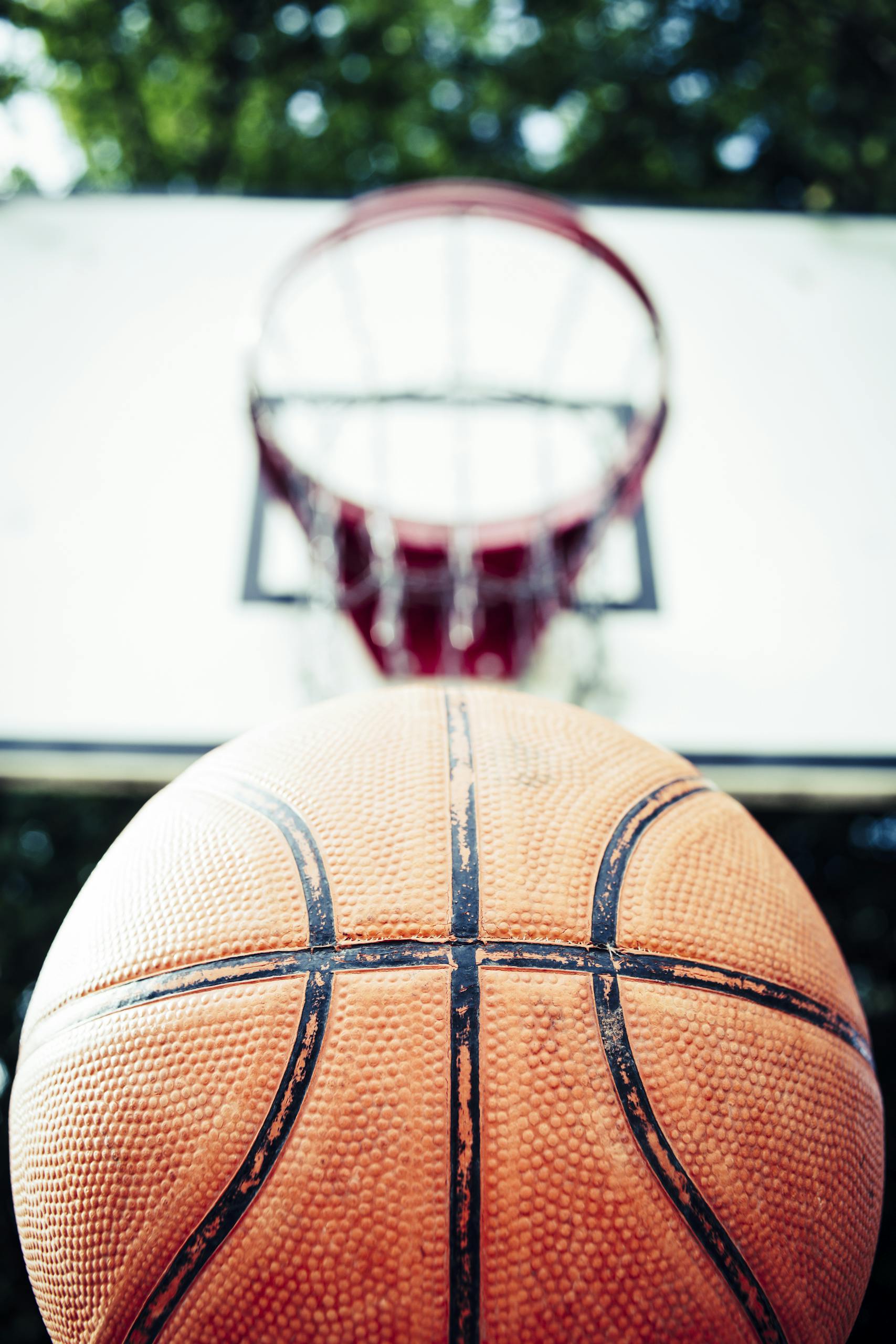 Vivid image of a basketball aiming for a hoop outdoors in daylight.